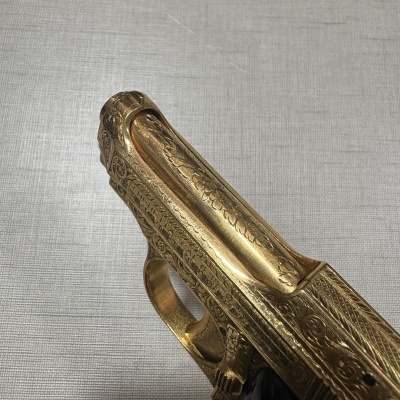 Pistola decorativa dourada com gravações detalhadas e punho preto