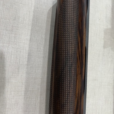 Objeto de madeira escura com padrão texturizado sobre fundo de tecido cinza claro