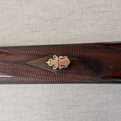 Cabo de arma de fogo em madeira escura com padrão quadriculado e emblema dourado