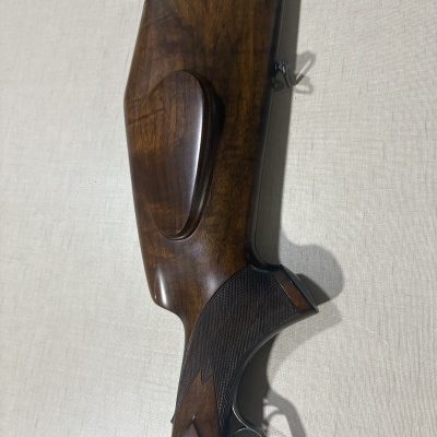 Coronha de madeira polida de um rifle com gravação metálica e acabamento quadriculado