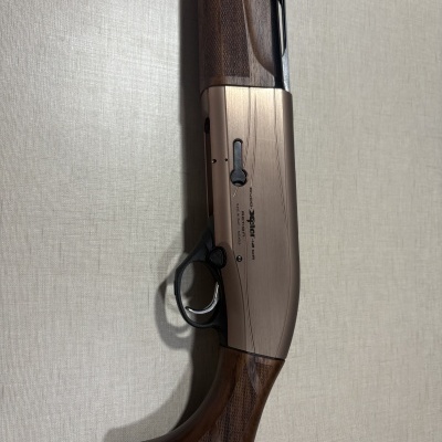 Arma de caça com coronha de madeira e corpo metálico bronze com texto, em cima de tecido claro.