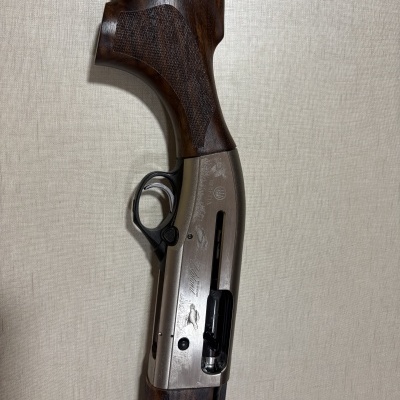 Espingarda de caça com coronha em madeira escura e corpo em metal prateado com gravações de patos e texto