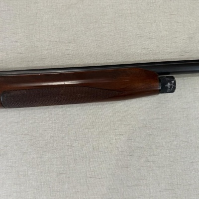 Espingarda com cano preto e punho de madeira castanha sobre tecido bege