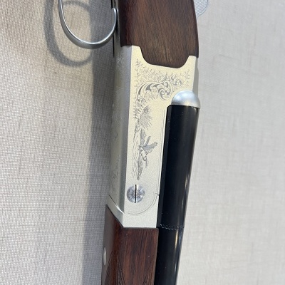 Parte de espingarda com madeira escura e metal gravado em fundo cinza