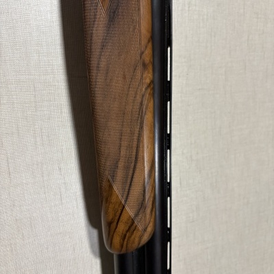 Caça espingarda com coronha de madeira castanha e cano metálico preto encostada a parede bege