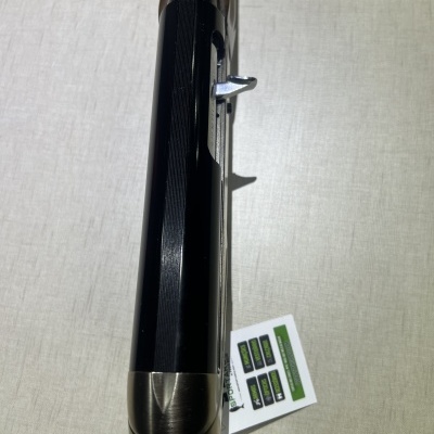 Arma de fogo com botão metálico prateado sobre superfície clara com etiqueta