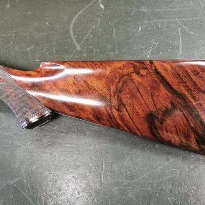 Coronha de espingarda de madeira polida com padrão natural castanho sobre superfície escura