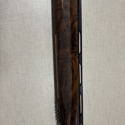 Parte dianteira de uma arma de fogo com detalhes em madeira escura e metal preto