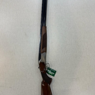 Espingarda com punho e coronha em madeira e canos metálicos escuros sobre superfície clara