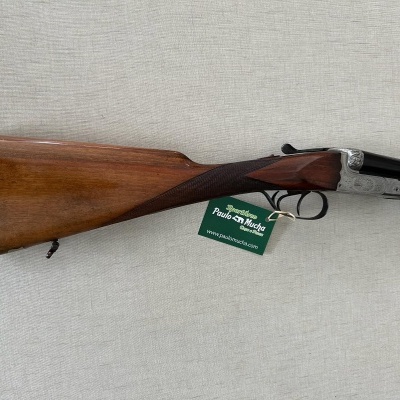 Espingarda de canos sobrepostos com coronha em madeira castanha e detalhes metálicos.