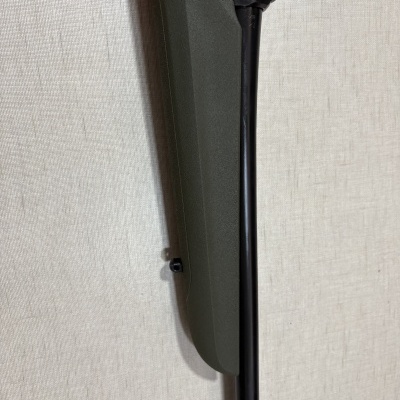 Espingarda com coronha verde-oliva e cano preto contra fundo bege.