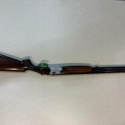 Espingarda de canos duplos dourada e madeira escura sobre fundo claro