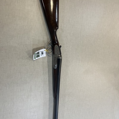 Espingarda de canos duplos com coronha em madeira escura e canos metálicos pretos pendurada na parede