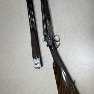 Espingarda de caça com coronha de madeira escura e canos duplos removidos sobre fundo claro