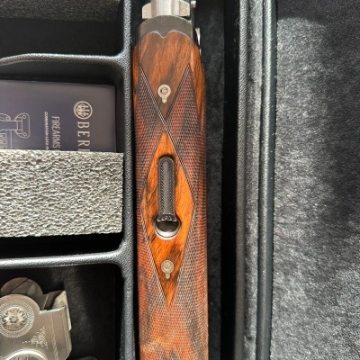 Arma de fogo com empunhadura em madeira com entalhes e parte metálica prateada em estojo preto aveludado