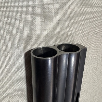 Detalhe das aberturas dos canos de arma de fogo em metal preto fosco sobre fundo bege texturado.