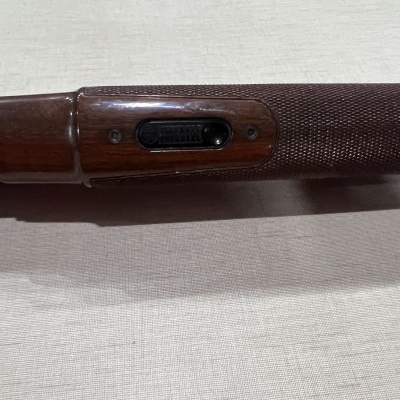 Coronha de espingarda de madeira castanha com peça metálica preta gravada 'REMINGTON' sobre tecido bege claro