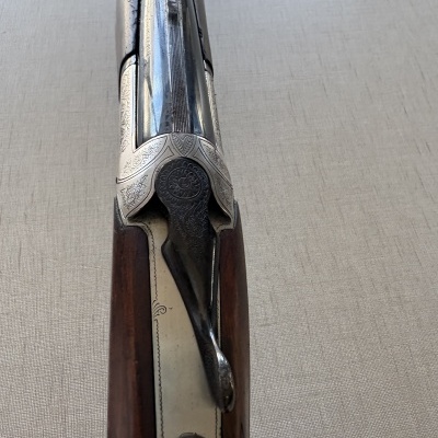 Espingarda com metal gravado e madeira sobre superfície cinza clara