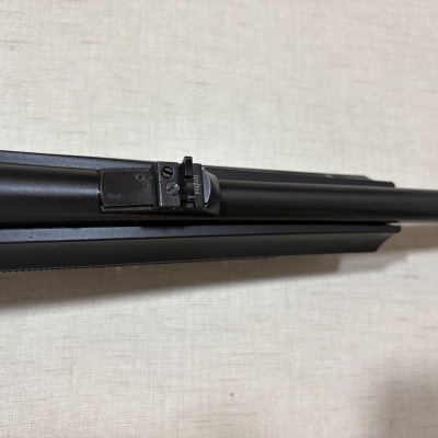 Cano negro de arma de fogo com mira traseira ajustável sobre fundo bege texturizado