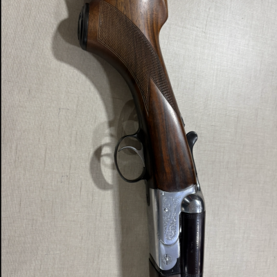 Espingarda de caça com madeira castanha e detalhes em metal prateado.