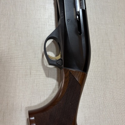 Parte de arma de fogo com punho em madeira castanha e parte metálica preta com gatilho dourado
