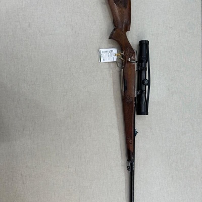 Carabina de madeira escura com luneta preta e etiqueta pendurada