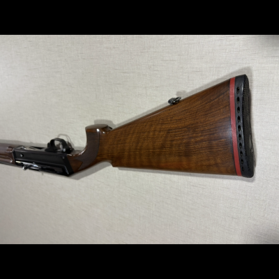 Espingarda com coronha em madeira castanha polida encostada a parede