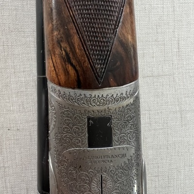 Detalhe de punho em madeira e corpo metálico gravado de arma de fogo