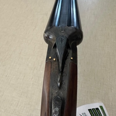 Espingarda de canos paralelos em metal preto e madeira castanha com detalhes gravados.