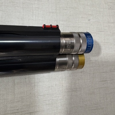 Extremidade de dois canos de arma com acabamento metálico, um com etiqueta azul BERETTA e outro amarelo