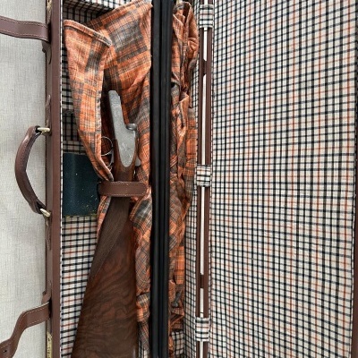 Mala aberta com espingarda desmontada e forro xadrez.