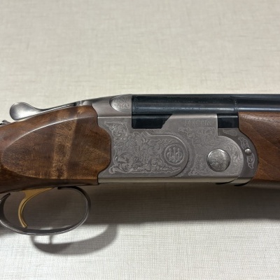 Espingarda de caça Beretta com coronha de madeira castanha e corpo metálico gravado.
