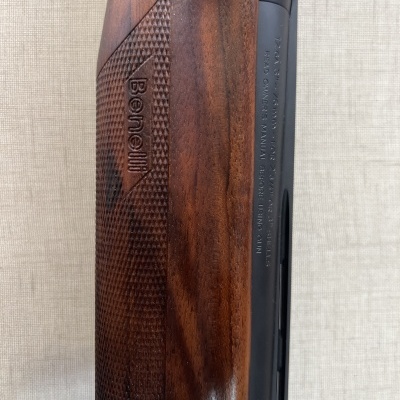 Detalhe de empunhadura em madeira com logo Benelli em arma de fogo
