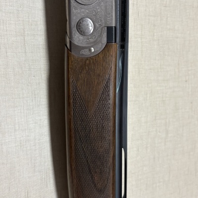 Espingarda Beretta com madeira castanha trabalhada e metal cinzento decorado.
