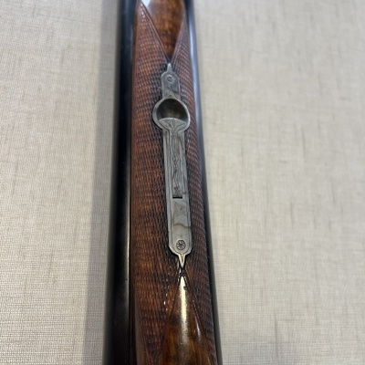 Espingarda com madeira polida castanha e metal decorado sobre tecido cinza