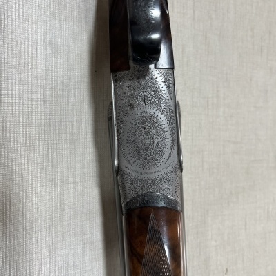 Arma de fogo com madeira escura e gravações metálicas ornamentais