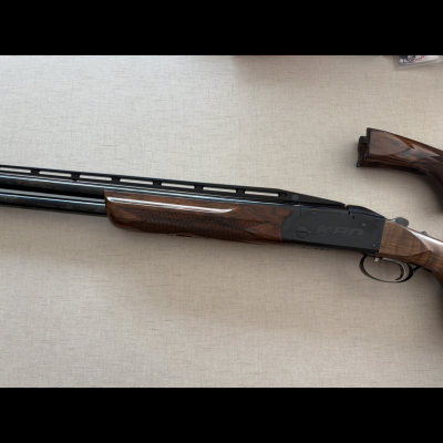 Espingarda de canos duplos em madeira castanha e metal preto sobre superfície cinza