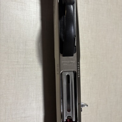 Arma de fogo metálica com cabo de madeira e textos gravados no metal