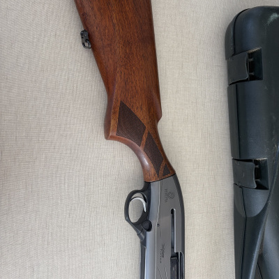 Espingarda semiautomática Beretta com coronha em madeira e metal cinza ao lado de estojo preto.