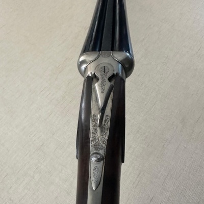 Espingarda de canos paralelos em metal preto e madeira escura com entalhes e detalhes metálicos gravados.