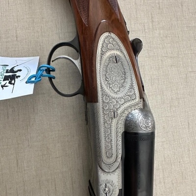 Espingarda de cano duplo com estrutura gravada e madeira castanha em fundo bege