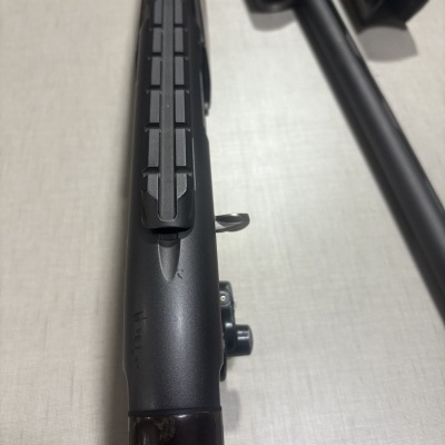 Rifle preto com partes em madeira escura sobre superfície clara texturada