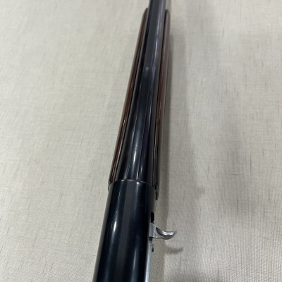 Cano de arma longa preta com gatilho prateado sobre superfície clara