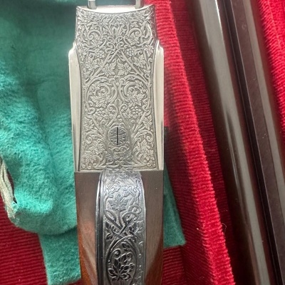 Arma de fogo com detalhes gravados, sobre caixa vermelha e verde