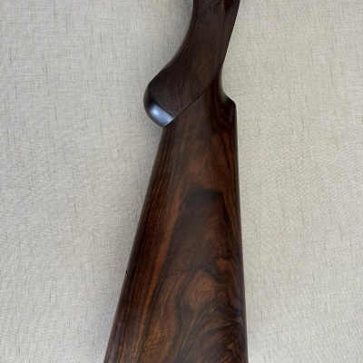 Coronha de arma de fogo em madeira escura polida com peça preta inferior, sobre fundo cinza claro