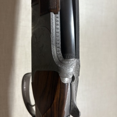 Espingarda com canos duplos em metal escuro e empunhadura em madeira polida com gravações decorativas.