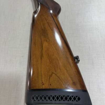 Cabo traseiro de arma de caça em madeira castanha polida com ponteira em borracha preta.