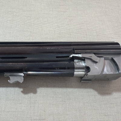 Parte superior e frontal de uma arma de fogo de canos paralelos em metal preto e cinzento