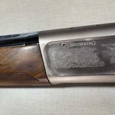 Parte lateral de espingarda com cabo em madeira e metal cinza com gravações decorativas e logo Browning