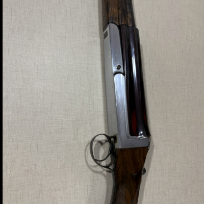 Espingarda com madeira castanha escura e metal prateado contra fundo bege